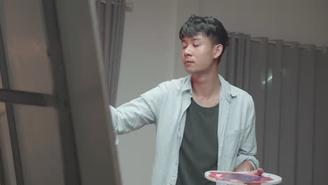 asian male artist painting and looking at his picture