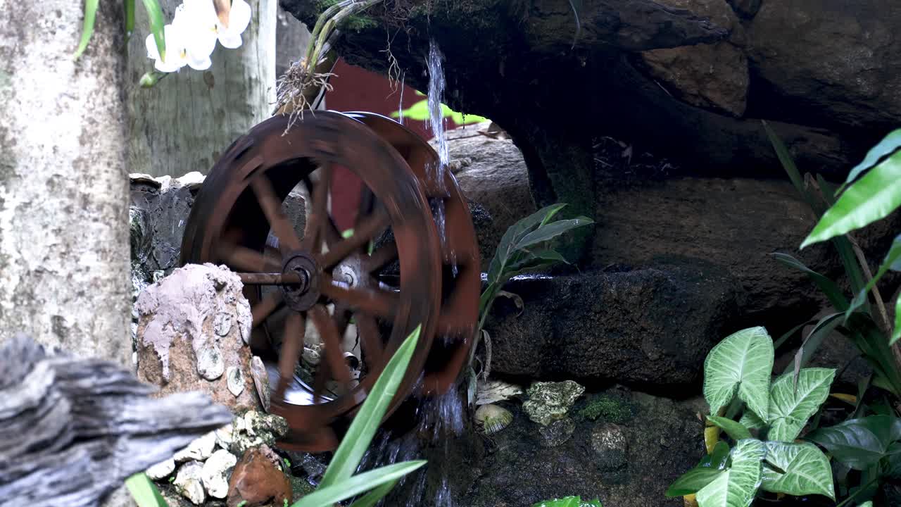 view of water wheel running at full speed in an indoor environment with pond and vegetation