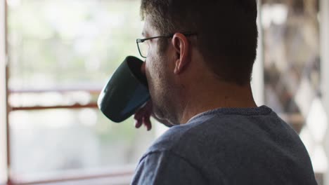 Thoughtful-caucasian-man-drinking-coffee-in-kitchen-at-home