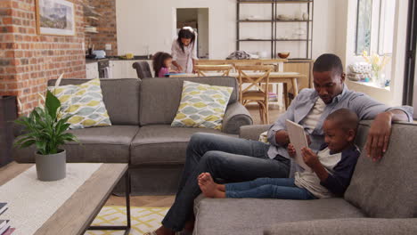 father and son sit on sofa in lounge using digital tablet