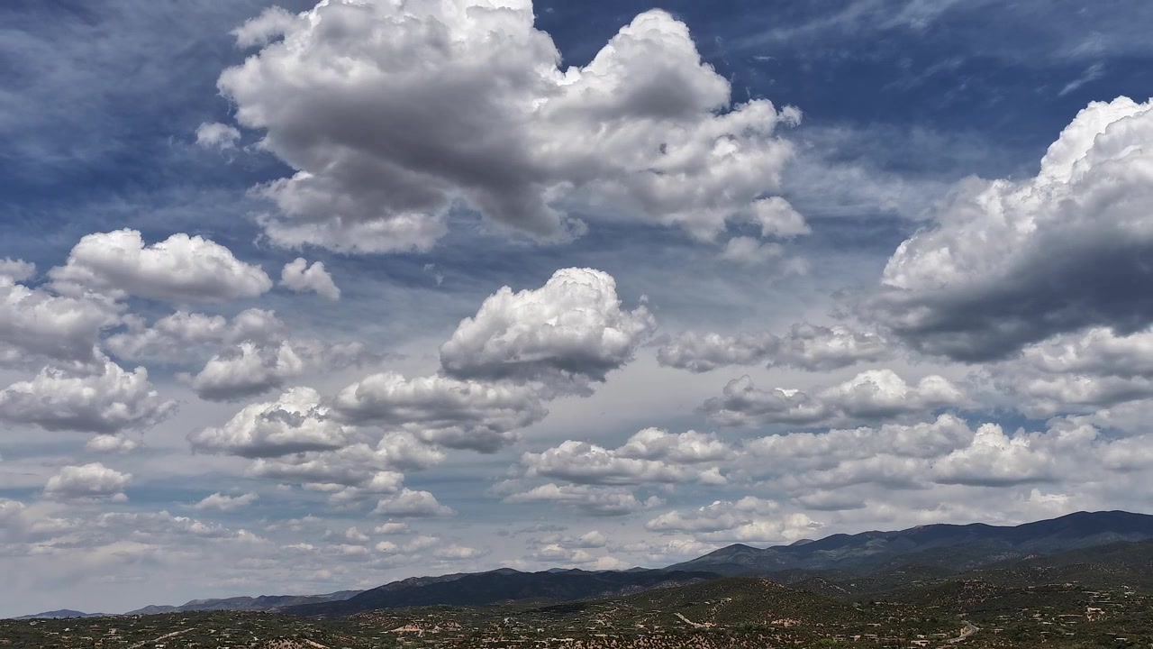 4K luftbåren timelapse fanger lag af bevægende pufskyer over de nordvestlige Santa Fe, New Mexico foden. Cinematisk droneoptagelse afslører plettede skygger, der ruller hen over det solbeskinnede terræn.