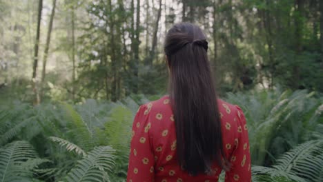 enchanted forest stroll: a woman in a vibrant red dress walking between thick, lush ferns in a vibrant green forest