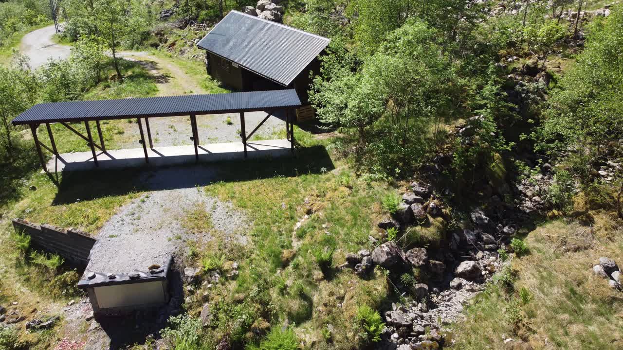 campo de tiro de pichón de arcilla en un remoto valle oculto - campo de tiro deportivo sin gente en un día soleado - cierre aéreo hasta lejos con inclinación hacia arriba para revelar el valle y el fondo