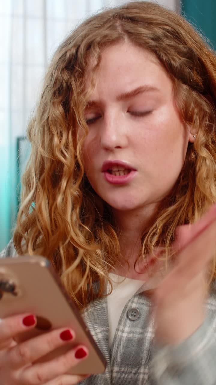 Young woman sits on sofa texting with anger waving hand annoyed by message using mobile phone chat