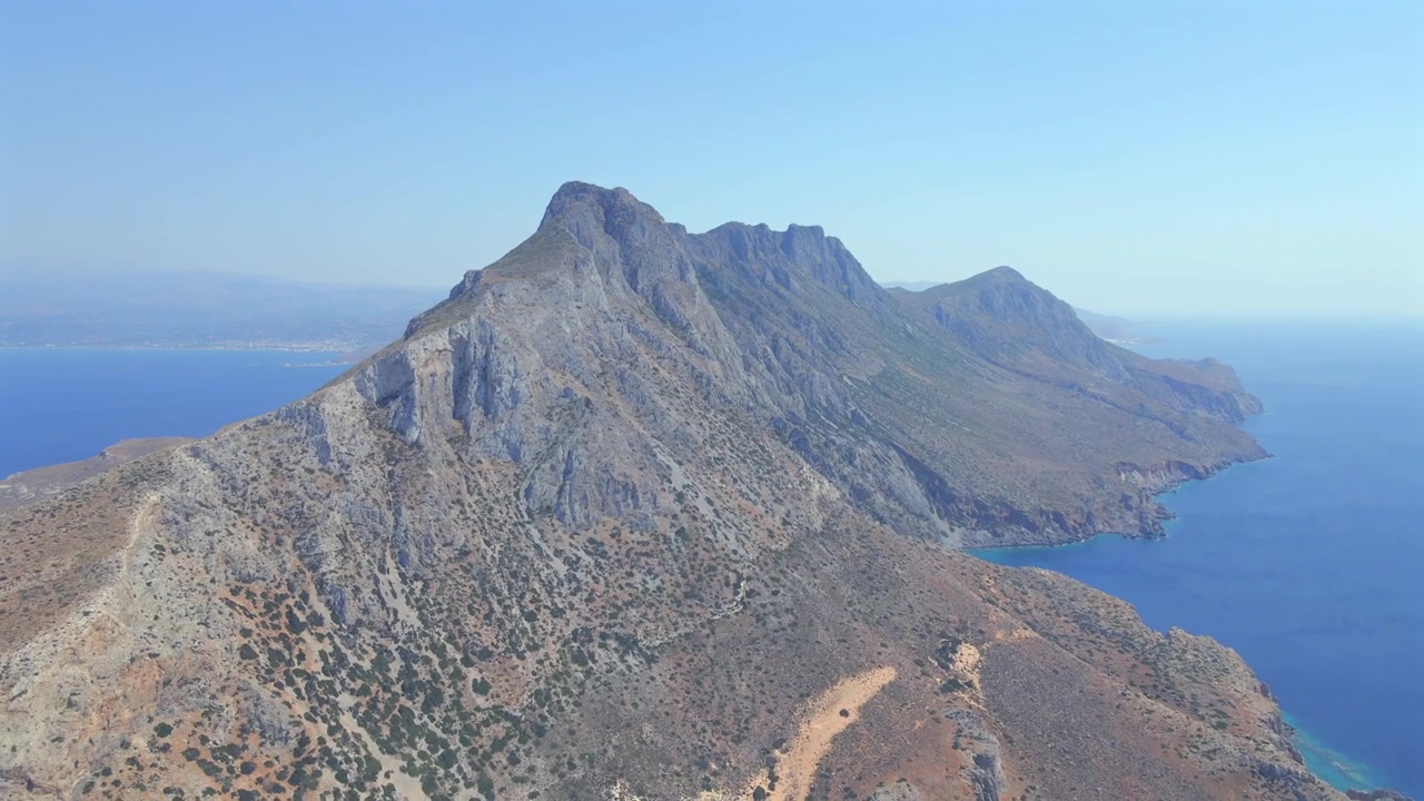 Spettacolare ripresa grandangolare con drone che cattura l'imponente catena montuosa della penisola di Gramvousa vicino a Balos a Creta, Grecia. Caratterizzata da un terreno aspro e arido circondato da acque marine di un blu intenso, in una giornata di sole.