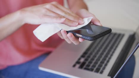 Mid-section-of-woman-wiping-her-smartphone-with-a-tissue