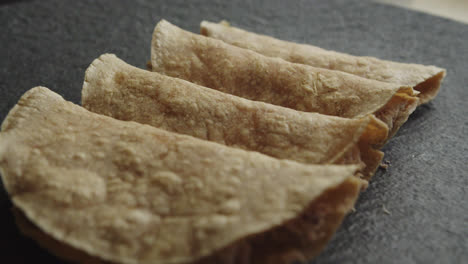 Beautiful-slow-motion-close-up-shot-with-slight-movement-of-a-group-of-chicken-chilaquiles-tacos-or-tortillas-on-a-black-plate-in-a-dimly-lit-industrial-kitchen