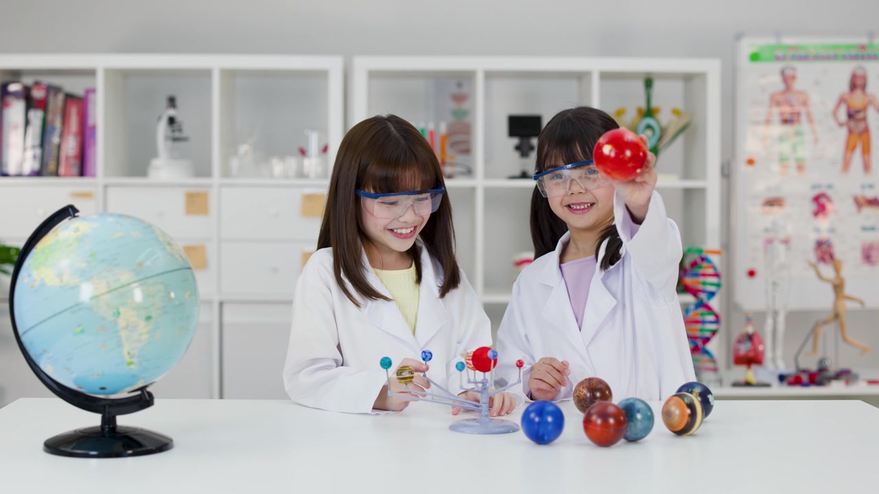 Two young students in safety goggles examine a planetary model in a bright science classroom.