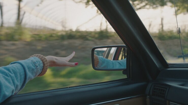 donna con la mano sul finestrino della macchina che sente il vento soffiare tra le dita che guida in campagna che viaggia in vacanza estiva viaggio su strada che gode della libertà sulla strada