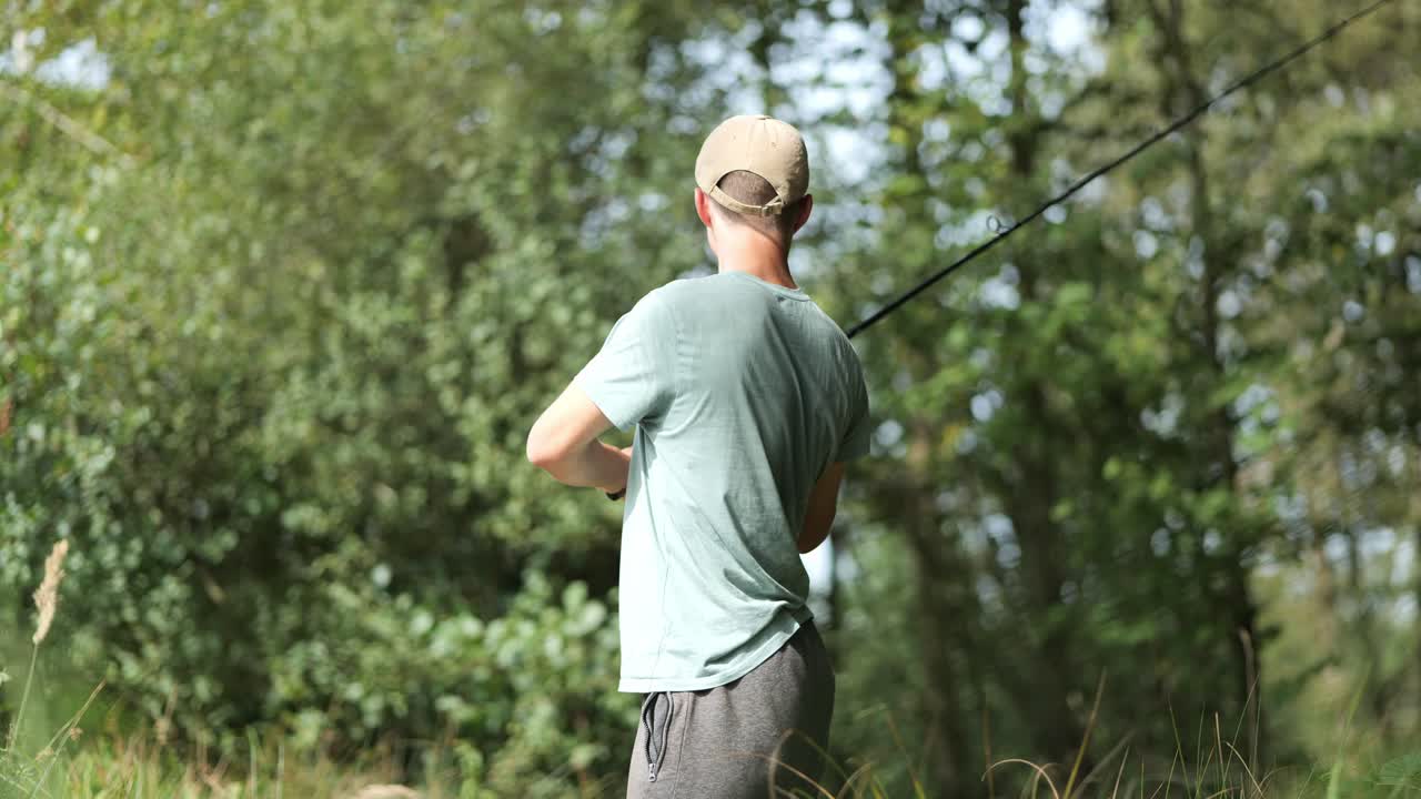 Young male angler stands at edge of forest throw fishing rod, concept of fishing as hobby