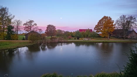 Lapso-De-Tiempo-Del-Amanecer-En-El-Lago-En-Un-Prado-Verde-Con-árboles-Y-Casas-De-Madera-Cielo-Con-Nubes-Avanzando-En-El-Tiempo