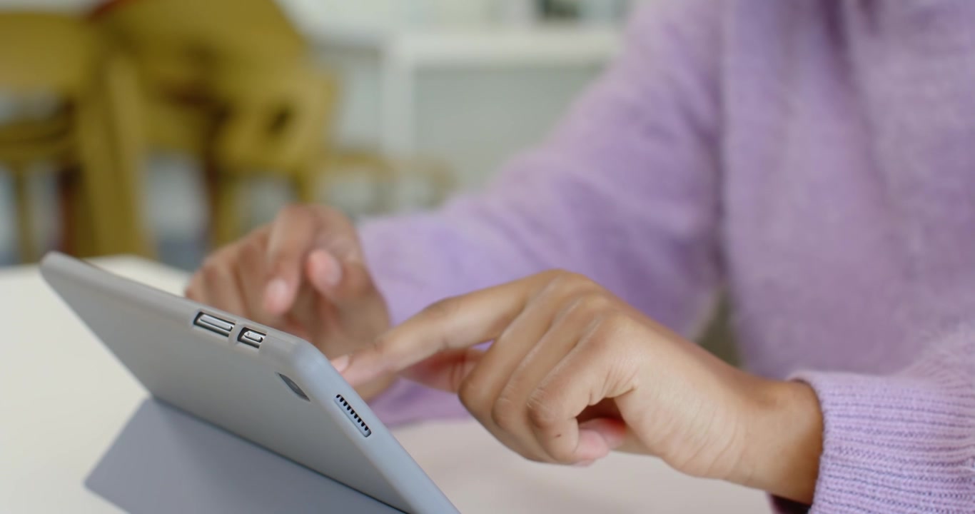 African female youth wearing lavender sleeve holding tablet on stand, tapping screen and browsing