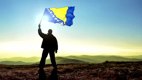 successful silhouette man winner waving bosnia and herzegovinaflag on top of the mountain peak. cinemagraph loop background