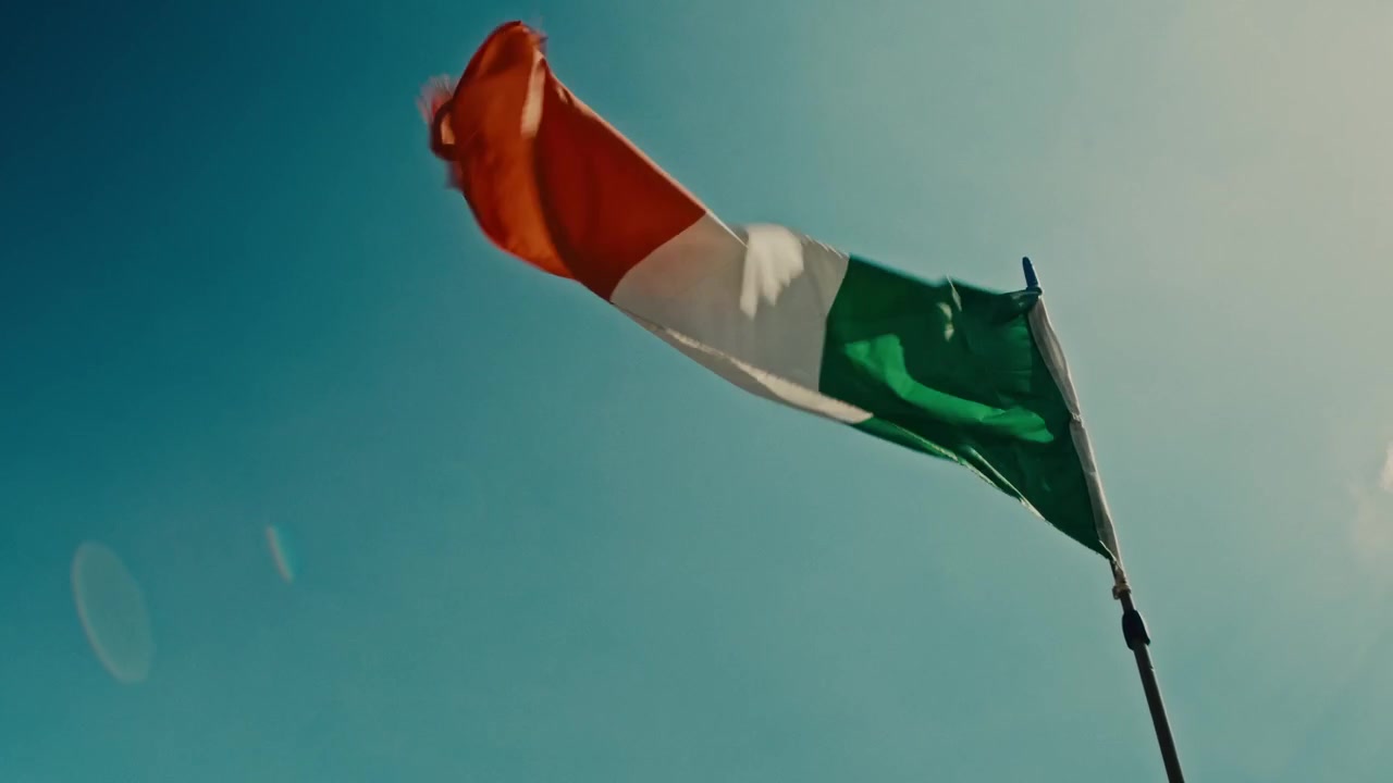Inquadratura dal basso della bandiera tricolore italiana che sventola contro un cielo azzurro limpido.