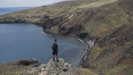 Man-stands-on-rock-overlooking-beautiful-small-bay-near-Ponta-de-São-Lourenço