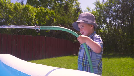 cute toddler boy filling a wading pool on a hot summer day