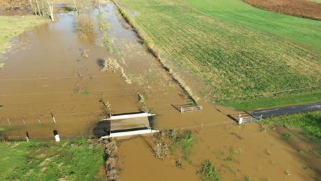 muddy flooded stream covers small bridge on farm lane, aerial view