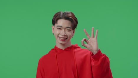 a portrait of a happy asian transgender male showing okay gesture to the camera in the green screen studio