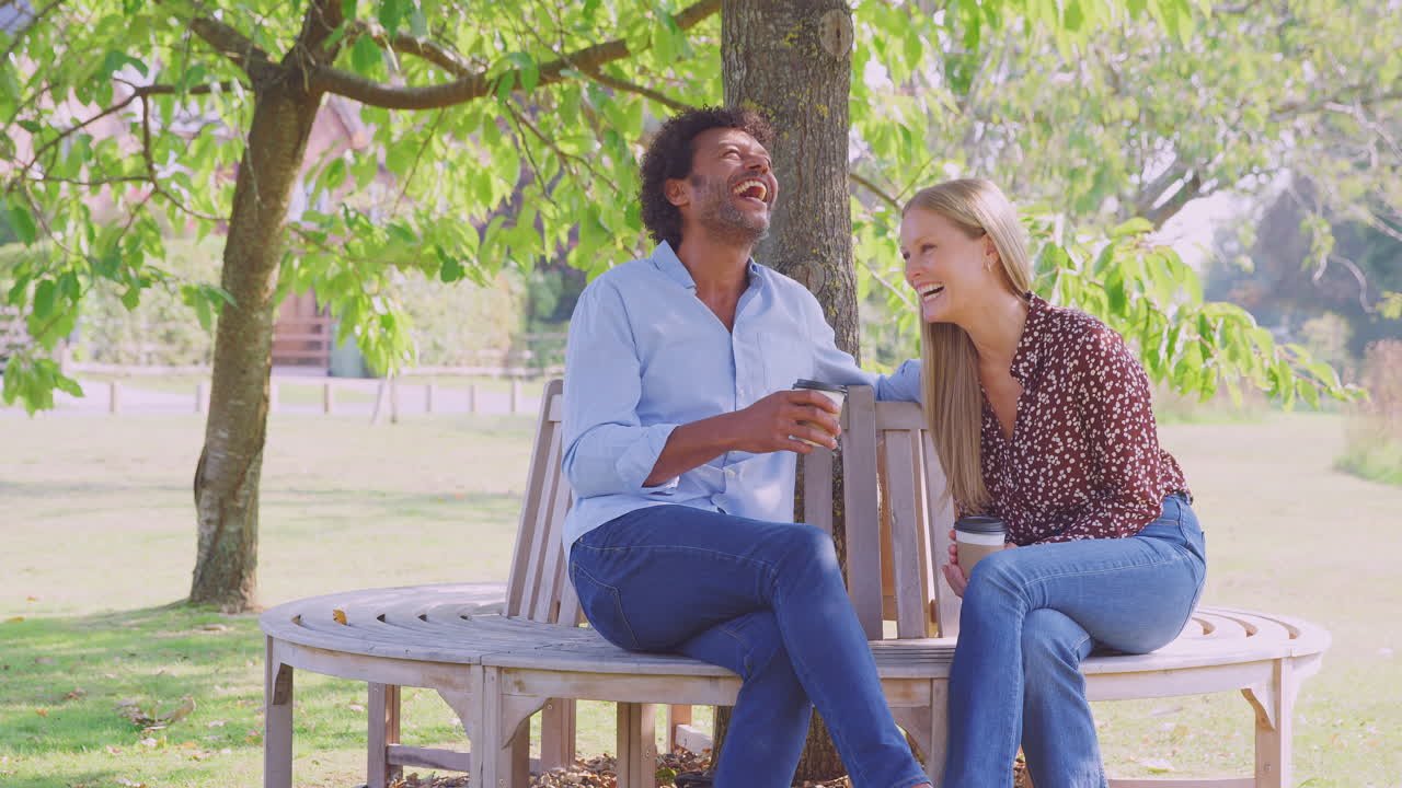 사랑하는 성숙한 커플이 커피를 마시며 여름 공원에서 나무 의 벤치에 함께 앉아 휴식을 취하고 있습니다.