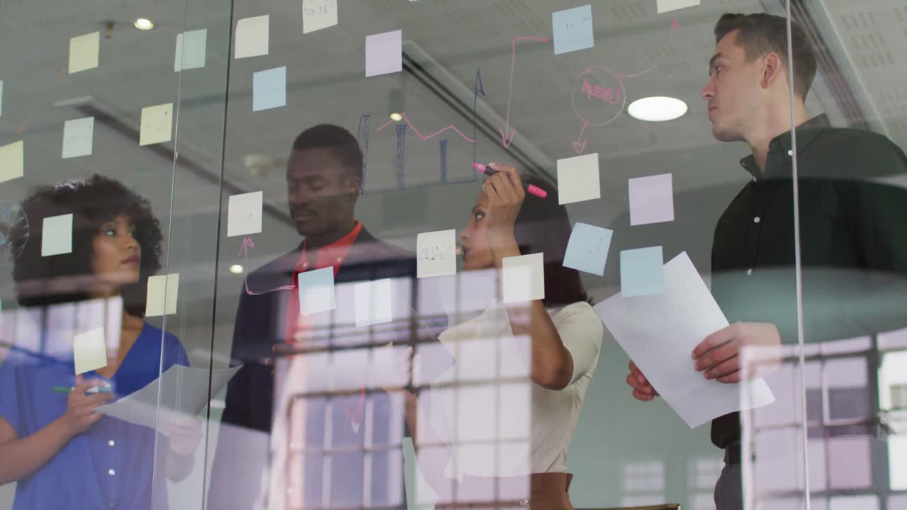 Diverse group of colleagues brainstorming in meeting room using glass wall