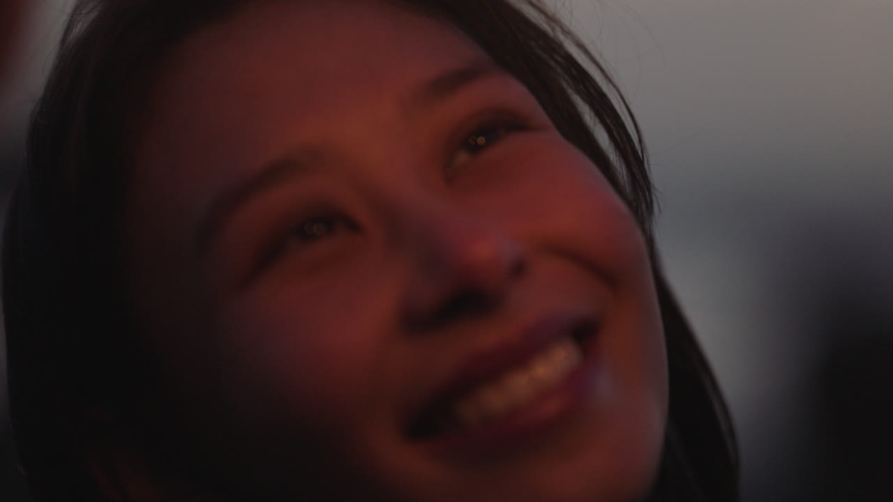 nahaufnahme von wunderkerzen, glückliche asiatische frau, die lächelnd silvester feiert und die feier zum unabhängigkeitstag am strand bei sonnenuntergang genießt