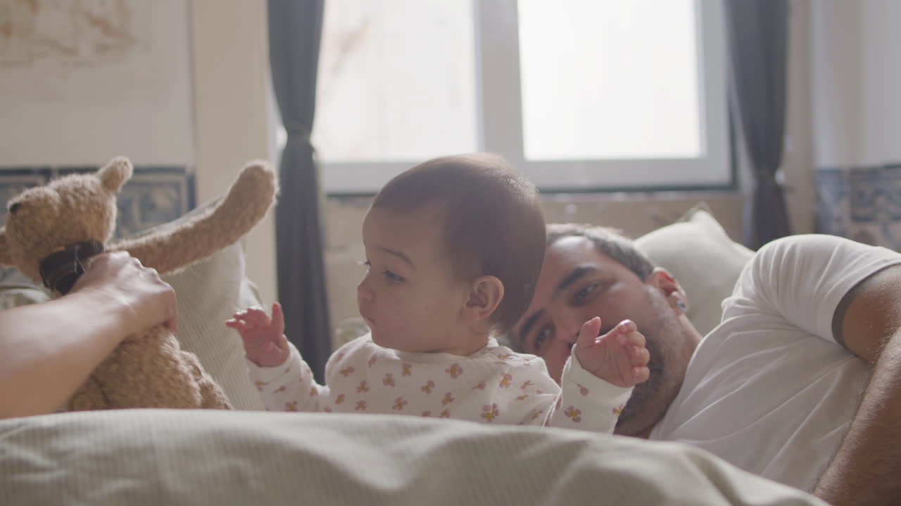 Happy Couple Lying In Bed On Sunday Morning And Playing With Their Cute Baby Girl