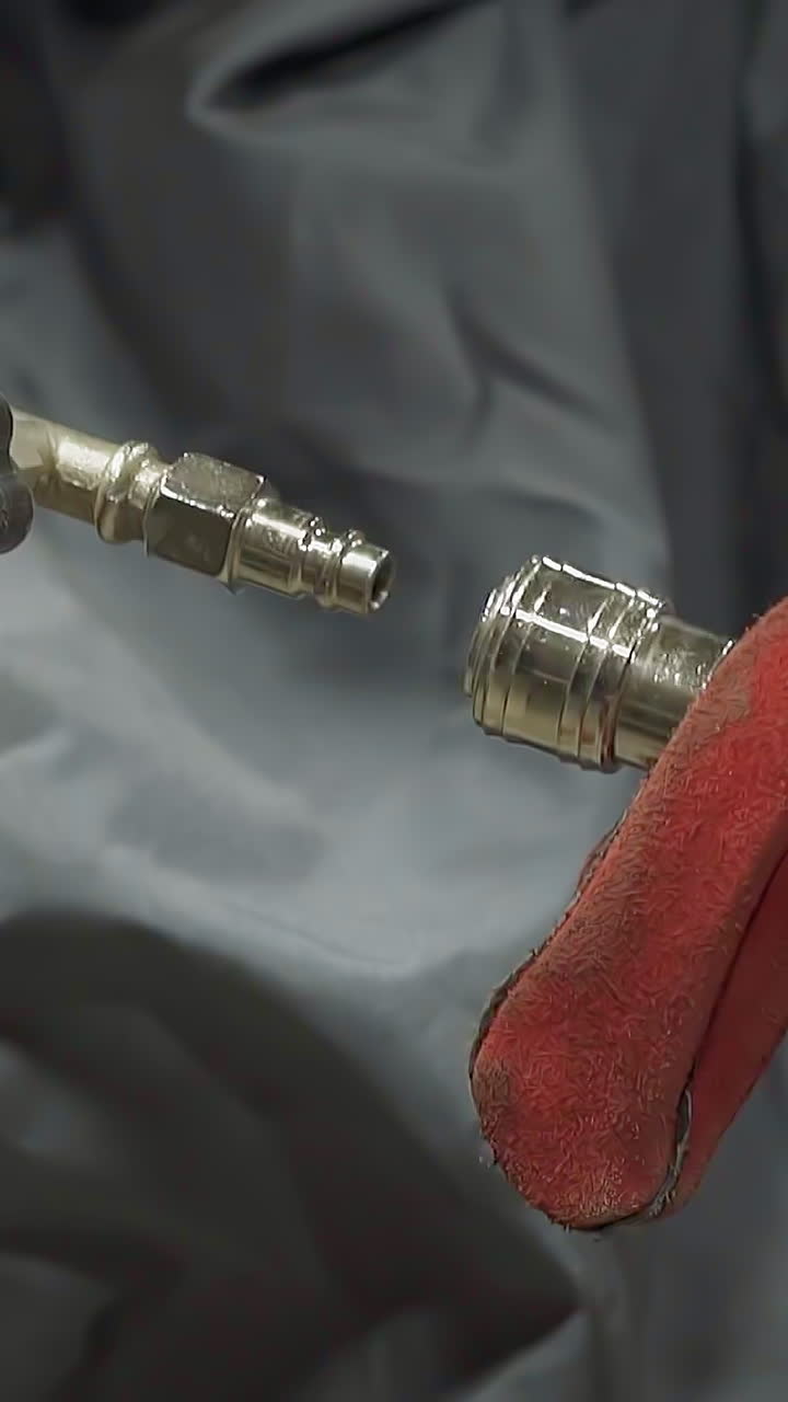 Worker with protective leather gloves connects metal pipes assembling equipment in workshop closeup. Employee adjusts instrument at production site