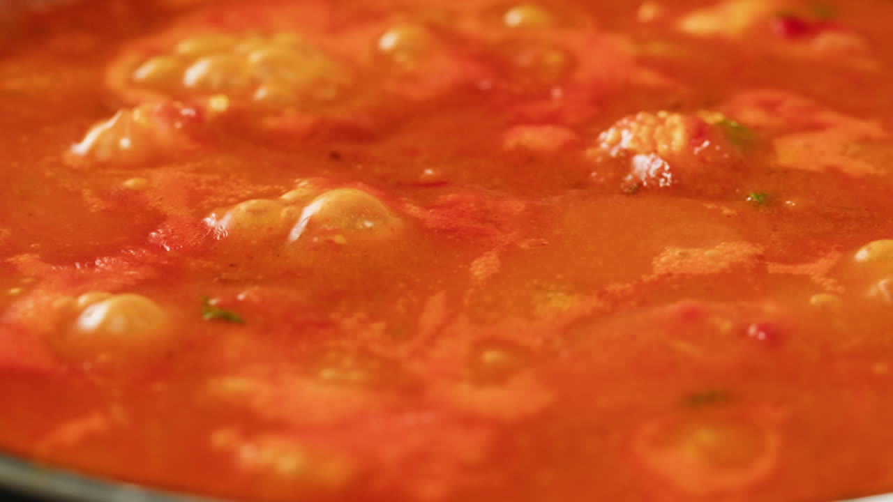 Chicken in tomato sauce is boiling on a frying pan with spices. Cooking tomato sauce curry with chicken fillet. Traditional Italian Mexican Asian dish. High quality studio shot for cafe, restaurant close up.