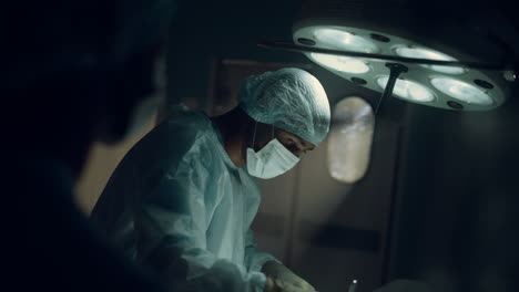 focused surgeon performing operation in dark sterile hospital operating room.