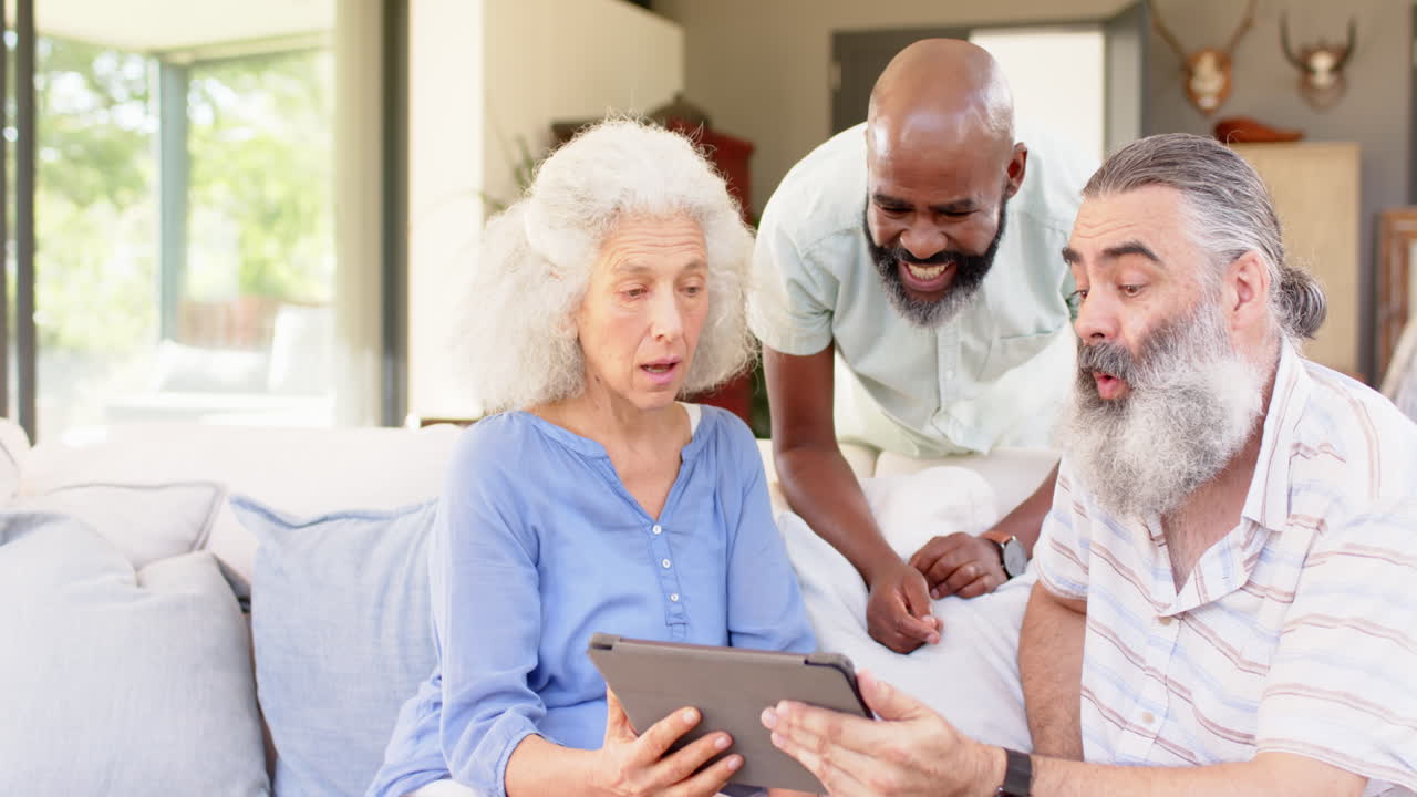 Amici anziani che usano il tablet, ridono e si godono il tempo insieme sul divano.