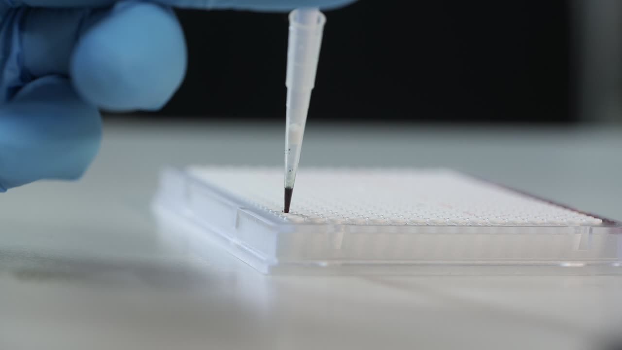 Highly detailed close-up of a micropipette tip carefully dispensing a small drop of liquid into a well plate