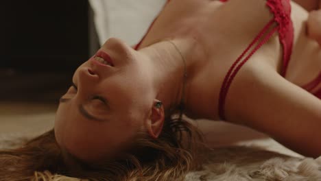close up of an attractive woman dressed in sexy red lingerie enticingly stroking her body and arching her back while lying on a fur rug