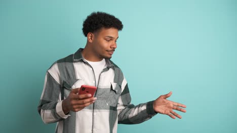 happy man using cellphone and pointing sideways in blue studio