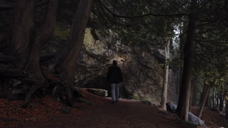 male hiker walking to the mouth of a cave situated at a limestone cliff, wide shot