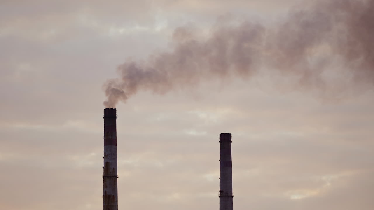 Industrial pipes with smoke against the evening sky. Harmful emissions released from industrial chimney. Air pollution.