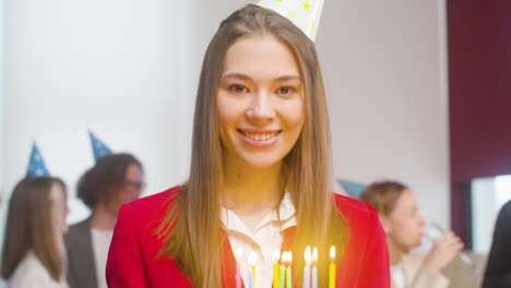 retrato de una hermosa mujer sosteniendo un pastel de cumpleaños y mirando a la cámara durante una fiesta en la oficina 1
