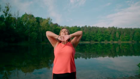 a caucasian woman in sportswear standing next to a lake and stretching body