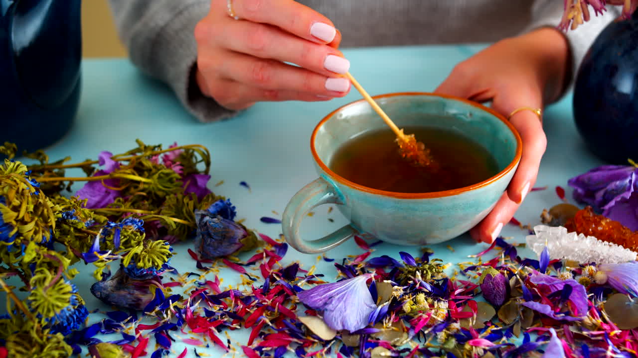 Female hands stirring tea with a stick of rock candy sugar in a ceramic cup. Surrounded by dried flowers, this cozy and tranquil scene is perfect for lifestyle, tea rituals, and relaxing content