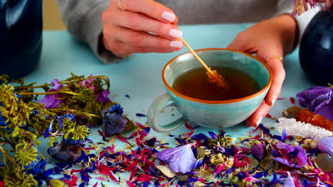 female hands stirring tea with a stick of rock candy sugar in a ceramic cup. surrounded by dried flowers, this cozy and tranquil scene is perfect for lifestyle, tea rituals, and relaxing content