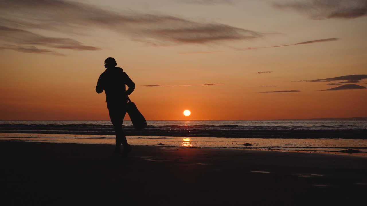 hombre corriendo con guitarra en la playa de arena trasera al atardecer