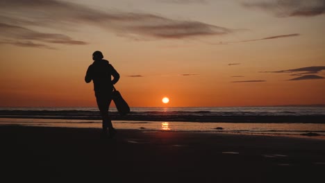 Man-running-with-guitar-in-back-sand-beach-at-sunset