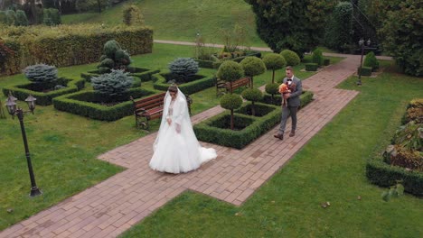 Newlyweds-bride-and-groom-with-bouquet-in-park,-wedding-couple-first-meeting,-aerial-drone-view