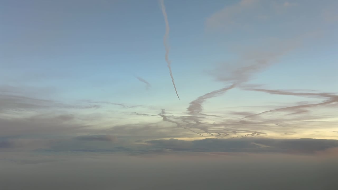 Immersive cockpit view flying at dawn in a serene pastel color sky, with some clouds in the horizon, and some jet contrails fading above in the upper atmosphere