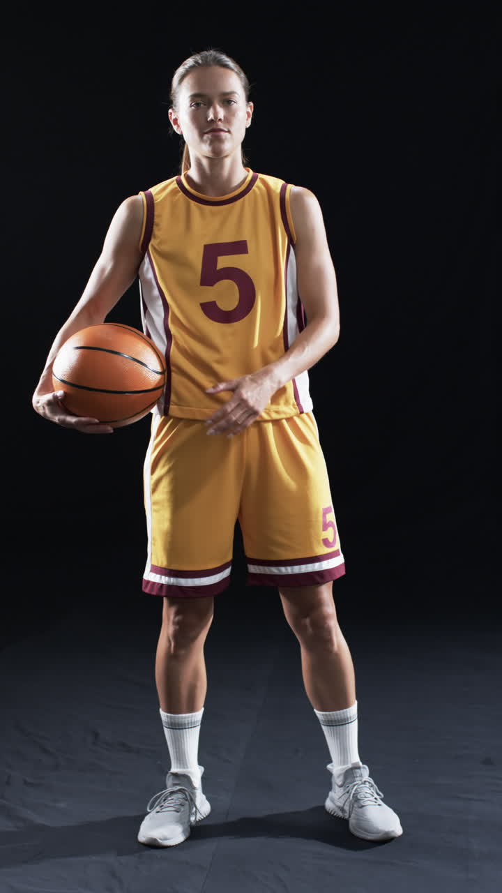 Vertical video: Holding basketball, strong and fit athlete in sports uniform posing confidently