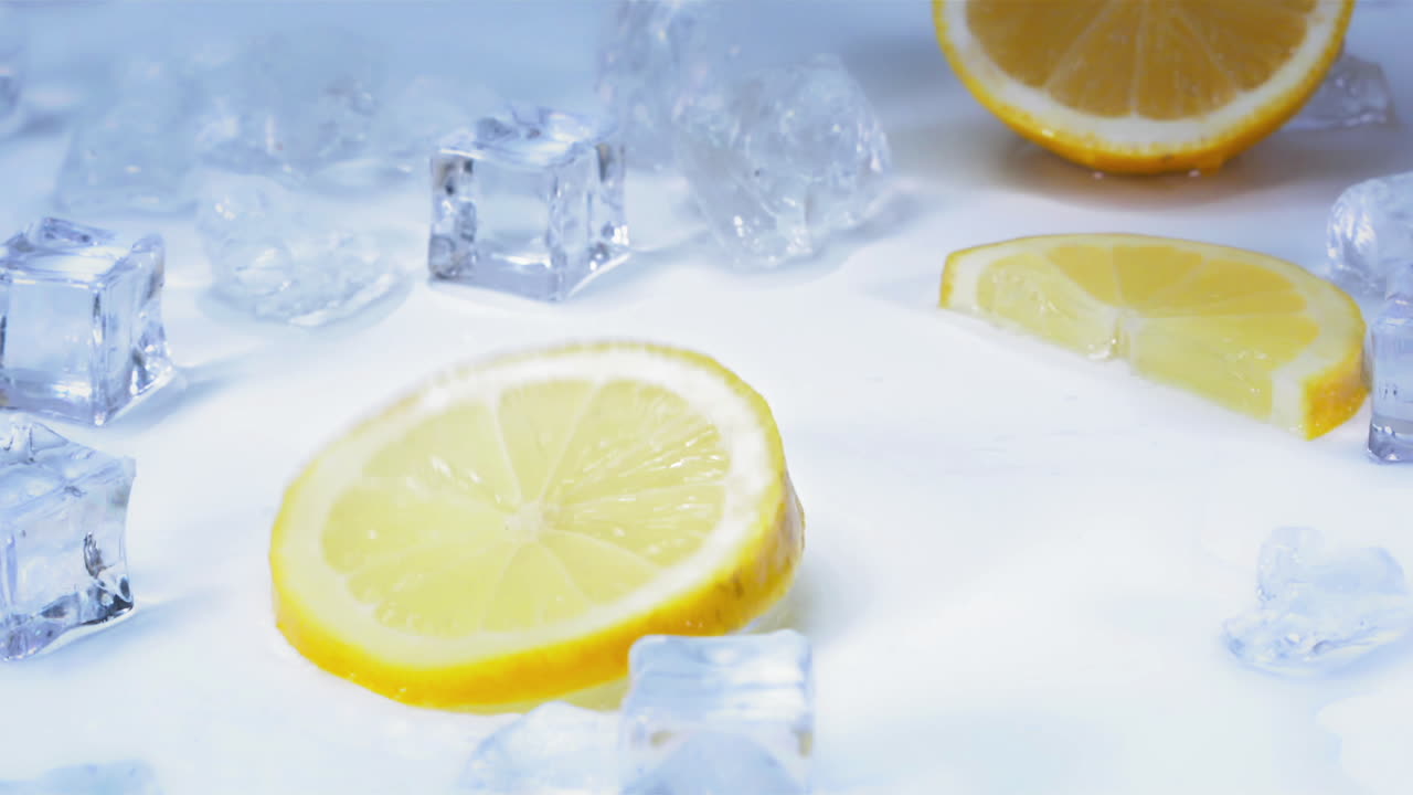 Movimento lento - Ripresa di una gustosa fetta di limone che ruota su un tavolo azzurro e bianco con cubetti di ghiaccio.
