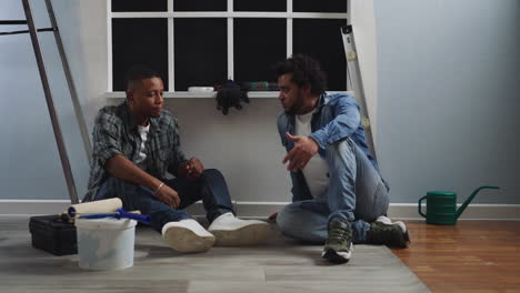 Tired-African-American-guys-talk-sitting-on-floor-at-window