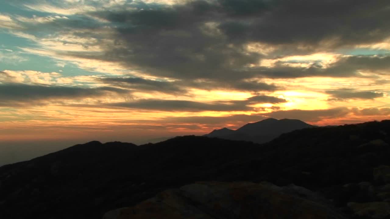 Panoramica a sinistra di uno scalatore in controluce appeso a una parete rocciosa strapiombante con il tramonto californiano sullo sfondo