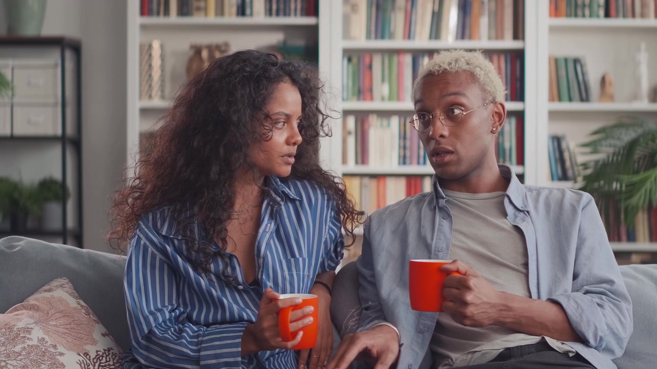 Et par bestående af en afrikansk mand og en indisk kvinde snakker på sofaen derhjemme.