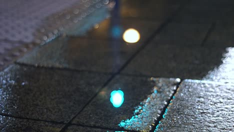 Puddle-reflecting-urban-sidewalk-traffic-lights-on-rainy-night