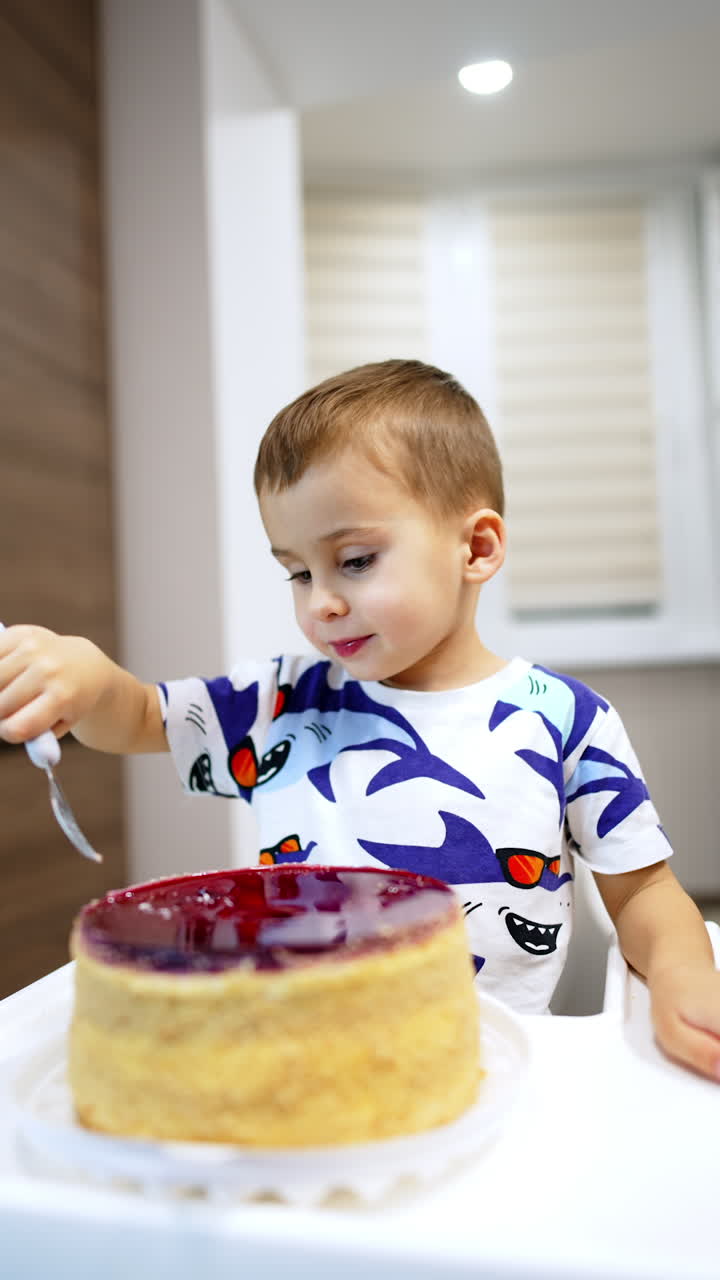 Adorable Caucasian toddler eating the whole cake with a fork. Happy kid enjoys dessert in the kitchen. Vertical video.